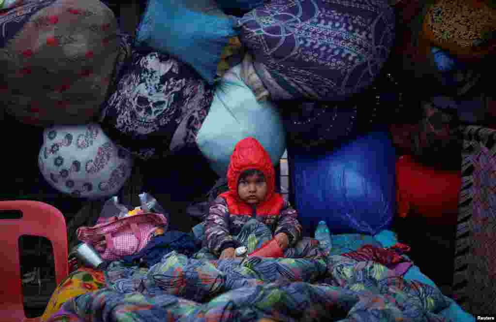 A boy wrapped in a quilt sits on a cot at a parking area on a cold winter morning in the old quarters of Delhi, India.