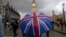 A pedestrian shelters from the rain beneath a Union Jack-themed umbrella near the Big Ben clock face and the Elizabeth Tower at the Houses of Parliament in central London, following the pro-Brexit result of the UK's EU referendum vote, June 25, 2016.