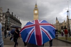 FILE - A pedestrian shelters from the rain beneath a Union Jack-themed umbrella near the Big Ben clock face and the Elizabeth Tower at the Houses of Parliament in central London, following the pro-Brexit result of the referendum vote, June 25, 2016.