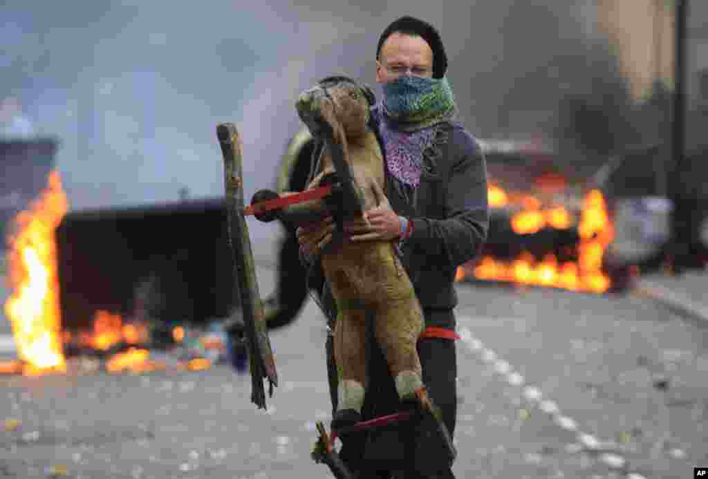 A masked man carries a toy backdropped by a burning car and garbage bins set on fire by rioters in Hackney, east London, Monday Aug. 8, 2011. Youths set fire to shops and vehicles in a host of areas of London _ which will host next summer's Olympic Game