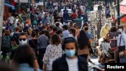 People wearing protective face masks walk in a busy street in Paris.