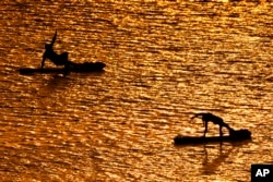 FILE - People do yoga poses on paddleboards at sunset at Olathe Lake on July 15, 2024, in Olathe, Kan. (AP Photo/Charlie Riedel)