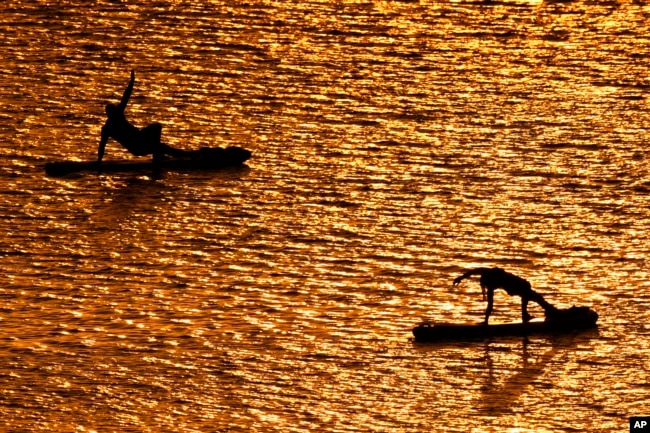 FILE - People do yoga poses on paddleboards at sunset at Olathe Lake on July 15, 2024, in Olathe, Kan. (AP Photo/Charlie Riedel)