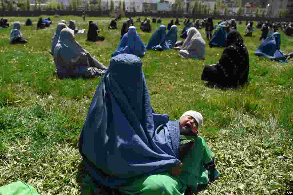 A woman wearing a burqa holds her child as she waits to receive free wheat from the Afghan government emergency committee during a government-ordered lockdown as a preventive measure against the coronavirus, in Kabul.