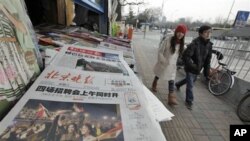 A Chinese couple walks past a newspaper front page showing Egyptians celebrating and title 'Mubarak hands over power' at a newsstand in Beijing, China, February 12, 2011