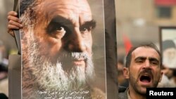 FILE - A man holds a picture of Ayatollah Ruhollah Khomeini, founder of the Islamic Republic as government supporters protest against opposition demonstrations during the holy day of Ashura, in Tehran, Dec. 30 2009. 