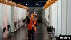 A helper gestures to send in three more patients to COVID-19 vaccination booths during the "Long Night of Vaccination", which featured DJs spinning tunes for attendees until midnight, at the Arena Treptow vaccination center in Berlin, Aug. 9, 2021.