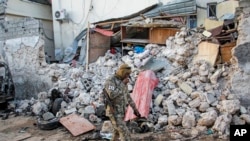 FILE - A soldier walks past wreckage after an attack on the Afrik hotel in Mogadishu, Somalia, Feb. 1, 2021. Though security forces eventually ended the attack, Somalia's government warned on Saturday that anyone who pays extortion money to al-Shabab would face legal action.