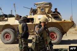 FILE - Afghan security forces stand near an armored vehicle during fighting between Afghan security forces and Taliban fighters in the Busharan area on the outskirts of Lashkar Gah, the capital of Helmand province, May 5, 2021.