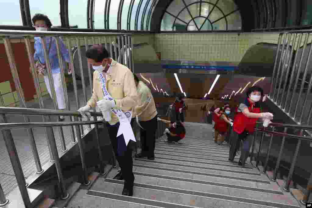 ماموران دولتی و داوطلبان در حال تمیز و ضدعفونی کردن میله‌ پله‌های یک ایستگاه مترو در کره جنوبی. بعد از شیوع کرونا، تمیز کردن اماکن عمومی به زندگی روزمره اضافه شده است. 