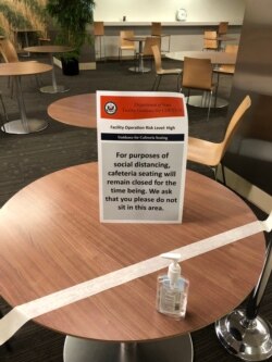 A sign on one of the tables in the State Department cafeteria that have been blocked off for weeks calls for social distancing. Facility operation risk level is marked as “high.” (Nike Ching/VOA)