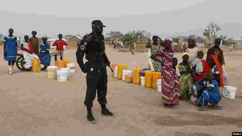 Un policier camerounais à côté des gens qui attendent de remplir leurs bidons d'eau dans un camp de réfugiés à Minawao au Cameroun, le 15 mars 2016.