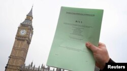 A journalist poses with a copy of the Brexit Article 50 bill, introduced by the government to seek parliamentary approval to start the process of leaving the European Union, in front of the Houses of Parliament in London, Jan. 26, 2017. 