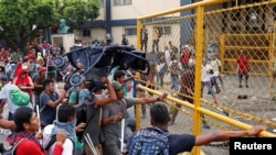 FILE - Central Americans, part of a caravan trying to reach the U.S., push the border gate during a protest as they try to cross into Mexico, in Tecun Uman, Guatemala, Oct. 28, 2018. The placard reads "We are not criminals we are migrants."