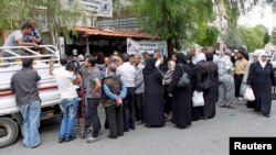 FILE - Displaced Syrians gather to collect food rations provided by the World Food Program (WFP) in front of a food distribution center in Damascus, October 2014.