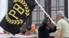 Un manifestante porta una bandera de los Proud Boys, un grupo de extrema derecha, mientras otgros miembros empiezan a desplegar una enorme bandera de Estados Unidos en una protesta frente a la legislatura del estado de Oregón a inicios de septiembre.