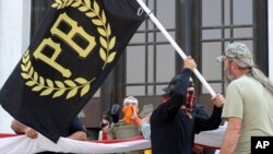 Un manifestante porta una bandera de los Proud Boys, un grupo de extrema derecha, mientras otgros miembros empiezan a desplegar una enorme bandera de Estados Unidos en una protesta frente a la legislatura del estado de Oregón a inicios de septiembre.