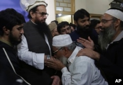 FILE - Supporters of Hafiz Saeed, second from left, head of the Pakistani religious party, Jamaat-ud-Dawa, kiss his hands as he arrived at a mosque in Lahore, Pakistan, Nov. 24, 2017.