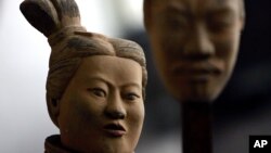 A female terracotta soldier statue holds the mask of a man as it stands in the midst of a terracotta army made up entirely of women and children at a gallery in Beijing's trendy art district, China Saturday Feb. 24, 2007. 