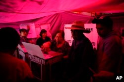 A woman casts her vote inside a polling station covered by a red tarp, during general elections in Iztapalapa, Mexico City, Sunday, July 1, 2018.