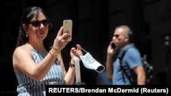 Seorang turis melepas maskernya saat berswafoto di Wall Street, New York, pada hari pertama pelonggaran aturan terkait pandemi COVID-19, 16 JUNI 2021. (Foto: Brendan McDermid/Reuters)
