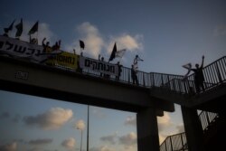 Israeli protesters hold flags and signs as they stand on a bridge to demonstrate against Prime Minister Benjamin Netanyahu in Hadera, Israel, Aug. 8, 2020. One sign in Hebrew reads: "Disconnected."