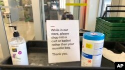 In this Sunday, March 29, 2020, photo, a sign posted at an entrance to a 365 Whole Foods store advises customers not to use their own bags while shopping in Lake Oswego, Ore. (AP Photo/Gillian Flaccus)