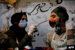 Palestinian artist Samah Said (L) paints an N95 protective mask worn by fellow artist Dorgham Krakeh (R) for a project raising awareness about the COVID-19 coronavirus pandemic, in Gaza City on March 24, 2020.