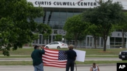 Warga memegang papan dan bendera AS di seberang jalan Curtis Culwell Center, di mana dua pria melepaskan tembakan di luar berlangsungnya acara kontes kartun Nabi Muhammad, di Garland, Texas (5/4).