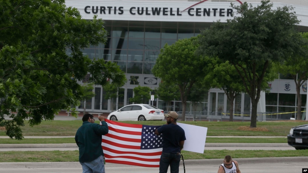 FILE - Men hold a sign and a U.S. flag across the street from the Curtis Culwell Center, where two men opened fire at an event soliciting cartoons of the Prophet Mohammad, in Garland, Texas, May 5, 2015.