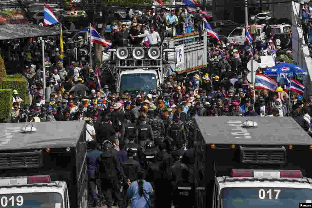 Riot police and soldiers stand guard as anti-government protesters gather at the gates of the Army Club where Prime Minister Yingluck Shinawatra was holding a meeting in Bangkok, Jan. 28, 2014.