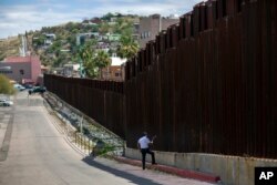 FILE - A man in Nogales, Arizona, talks to relatives standing on the other side of the border fence in Nogales, Mexico, April 1, 2017. Under President Donald Trump's plan, fenced sections of the U.S.-Mexican border would be secured with a wall.