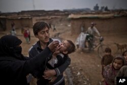 FILE - A Pakistani health worker, left, gives a polio vaccine to a child in a poor neighborhood that hosts people displaced from tribal areas and Afghan refugees, on the outskirts of Islamabad, Pakistan, Jan. 22, 2014.