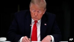 President Donald Trump signs his name on a piece of paper during a roundtable with governors on the reopening of America's small businesses, in the State Dining Room of the White House, June 18, 2020, in Washington. 