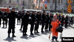 FILE - A sweeper walks past police officers as they stand guard during a rally of Russian opposition supporters in Moscow, May 6, 2017.