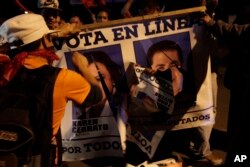 Anti-government demonstrators shatter a campaign poster of the National Party with a portrait of Honduran President Juan Orlando Hernandez during a march at the Morazan street in Tegucigalpa, Honduras, Dec. 8, 2017.