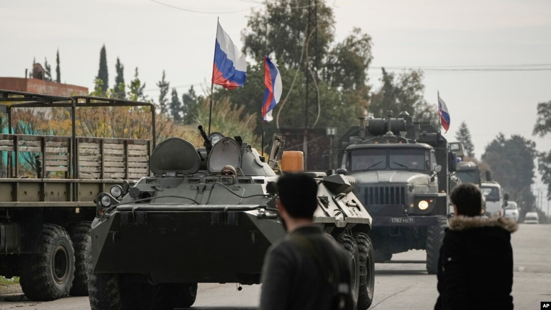 Sirijski borci posmatraju ruska vozila koja prolaze pored Hmeimim vazdušne baze, kojom trenutno upravlja Rusija, jugoistočno od Latakije, 16. decembra 2024. (Foto: AP/Leo Correa)