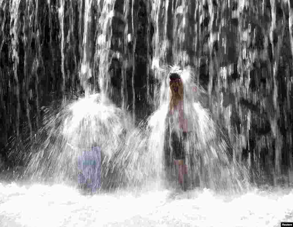 Pria Afghanistan berendam di bawah air terjun di provinsi Parwan, Afghanistan .