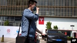 A man wears a mask as he walks past a Tesla electric vehicle showroom and charging station in Beijing, China, April 14, 2017.