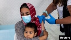 FILE - A migrant holds her baby as she receives a shot of the Johnson & Johnson vaccine against the coronavirus disease (COVID-19) in the Mavrovouni camp for refugees and migrants on the island of Lesbos, Greece, June 3, 2021.