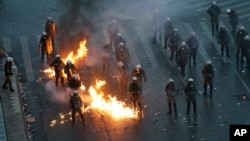 A molotov cocktail explodes next to Greek riot police during clashes after a rally in Athens, Jan. 20, 2019. 