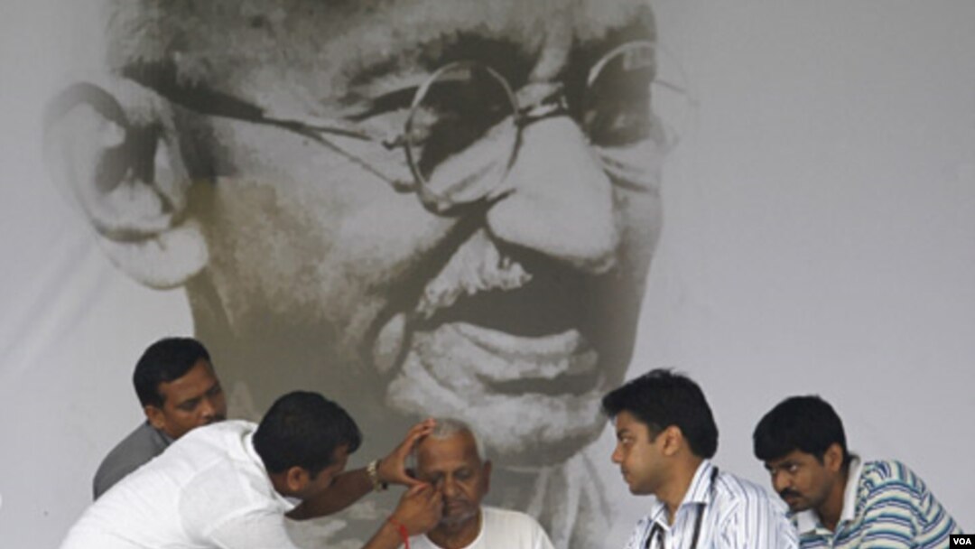 Tim dokter memeriksa aktivis Anna Hazare di depan potret raksasa Mahatma Gandhi, Selasa (23/8).