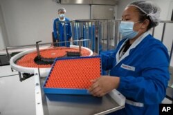 FILE - A worker feeds vials for production of SARS CoV-2 Vaccine for COVID-19 at the SinoVac vaccine factory in Beijing.
