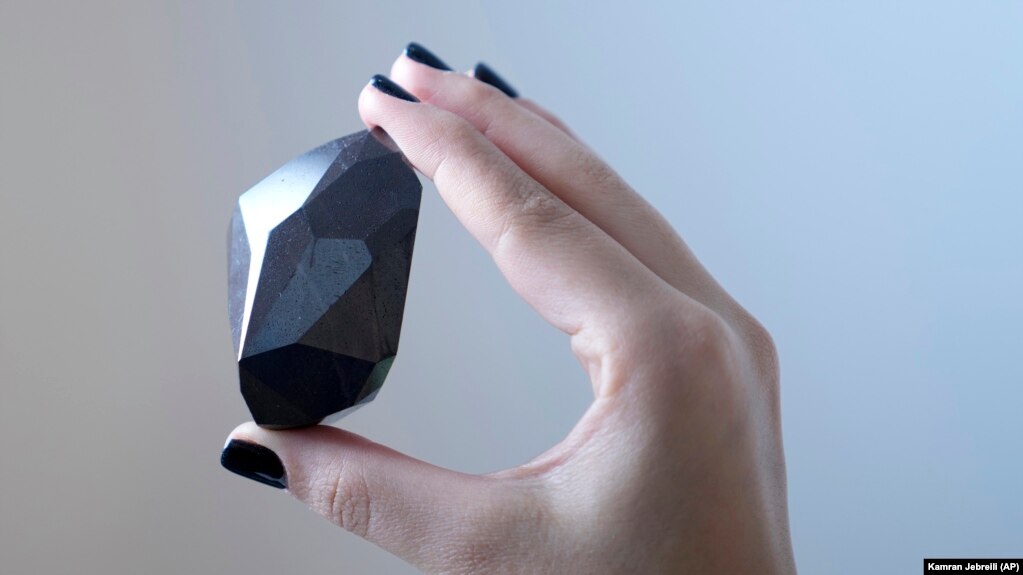 An employee of Sotheby's Dubai holds a 555.55 Carat Black Diamond called "The Enigma." Photo taken at Sotheby's Dubai gallery in Dubai, United Arab Emirates, January 17, 2022. (AP Photo/Kamran Jebreili)