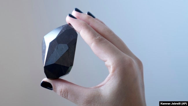 An employee of Sotheby's Dubai holds a 555.55 Carat Black Diamond called "The Enigma." Photo taken at Sotheby's Dubai gallery in Dubai, United Arab Emirates, January 17, 2022. (AP Photo/Kamran Jebreili)