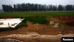 FILE - Broken pieces of glass protrude from a wall to keep out trespassers at an illegal golf course which was demolished and turned into a cornfield in the suburbs of Beijing, June 16, 2014.