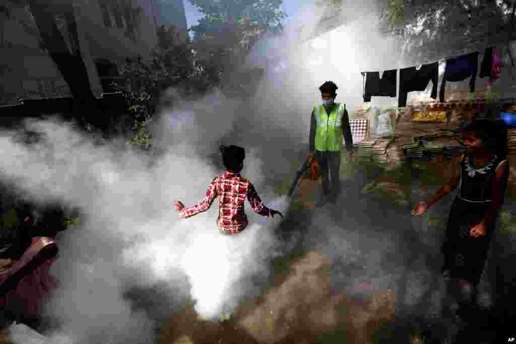 A boy plays in smoke from fumigation being carried out by a city worker at a housing area in Ahmedabad, India.