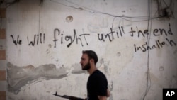 Un rebelde sirio en el distrito Amariya de Alepo. Fuerzas del gobierno y sus aliados cerraron hace poco la única vía hacia zonas bajo control rebelde en la ciudad. La leyenda en la pared dice "Lucharemos hasta el final. Si Dios quiere".