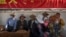 FILE - People rest in the shade under a government propaganda banner in Chinese and Tibetan in Lhasa, in China's Tibet Autonomous Region, on June 3, 2021. In a report released on May 22, 2024, Human Rights Watch says China is increasingly forcing rural Tibetans to move to cities.
