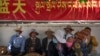 FILE - People rest in the shade beneath a government propaganda banner in Chinese and Tibetan near a neighborhood Tibetan Buddhist shrine in Lhasa, the capital of China's Tibet Autonomous Region, on June 3, 2021.